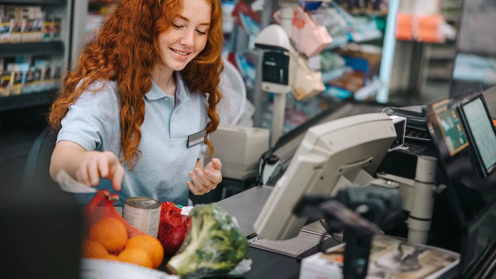 Jongere medewerkster achter de kassa van de supermarkt