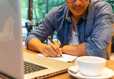 Man achter maakt aantekeningen achter zijn laptop