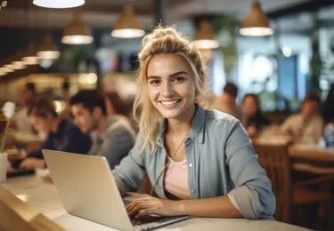 portret van jonge vrouw aan het werk achter laptop en kijkt lachend in de camera