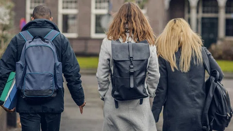 drie studenten met rugzakken en jassen aan. Hun ruggen naar de kijker gericht. In de herfst of winter.