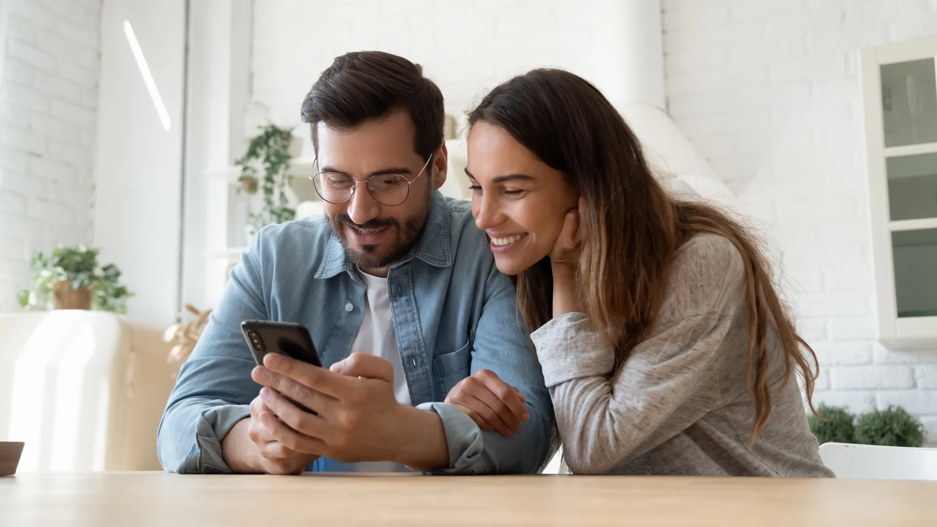 Een man en vrouw zitten aan tafel en kijken samen naar een telefoon