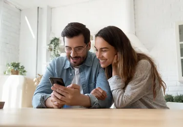 Een man en vrouw zitten aan tafel en kijken samen naar een telefoon