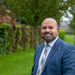 Abhilash staat buiten en is omringt met groen (bomen, struiken). Abhilash kijkt recht in de camera en glimlacht.