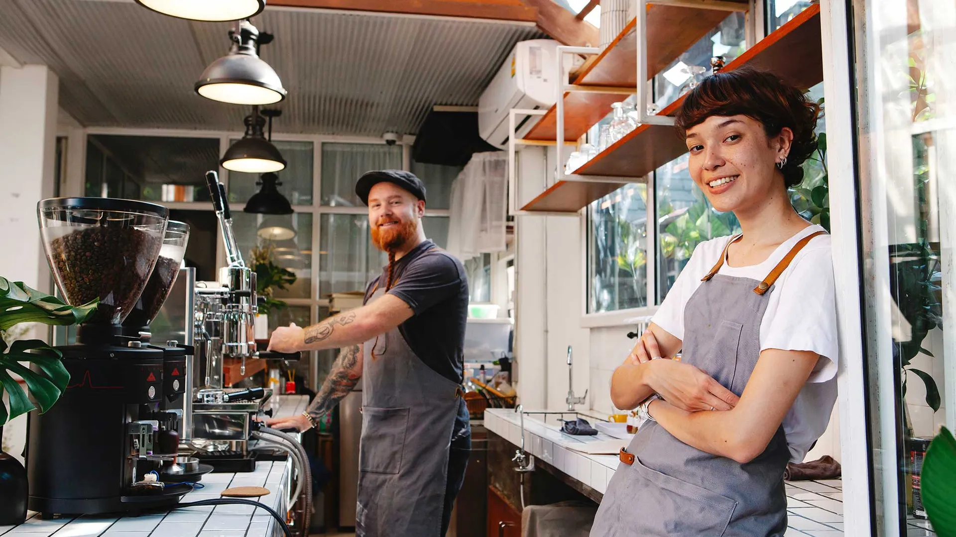 Twee horecamedewerkers staan achter de toonbank bij koffieapparaat.