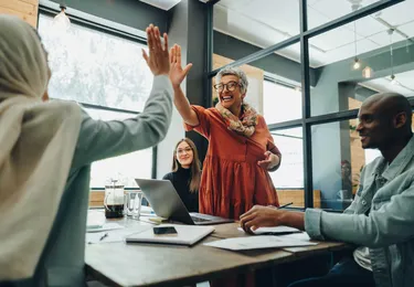 Collega's rondom tafel waar er twee een high five geven aan elkaar