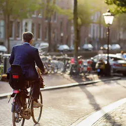 Man in pak op de fiets met kinderzitje op weg naar zijn werk in de binnenstad