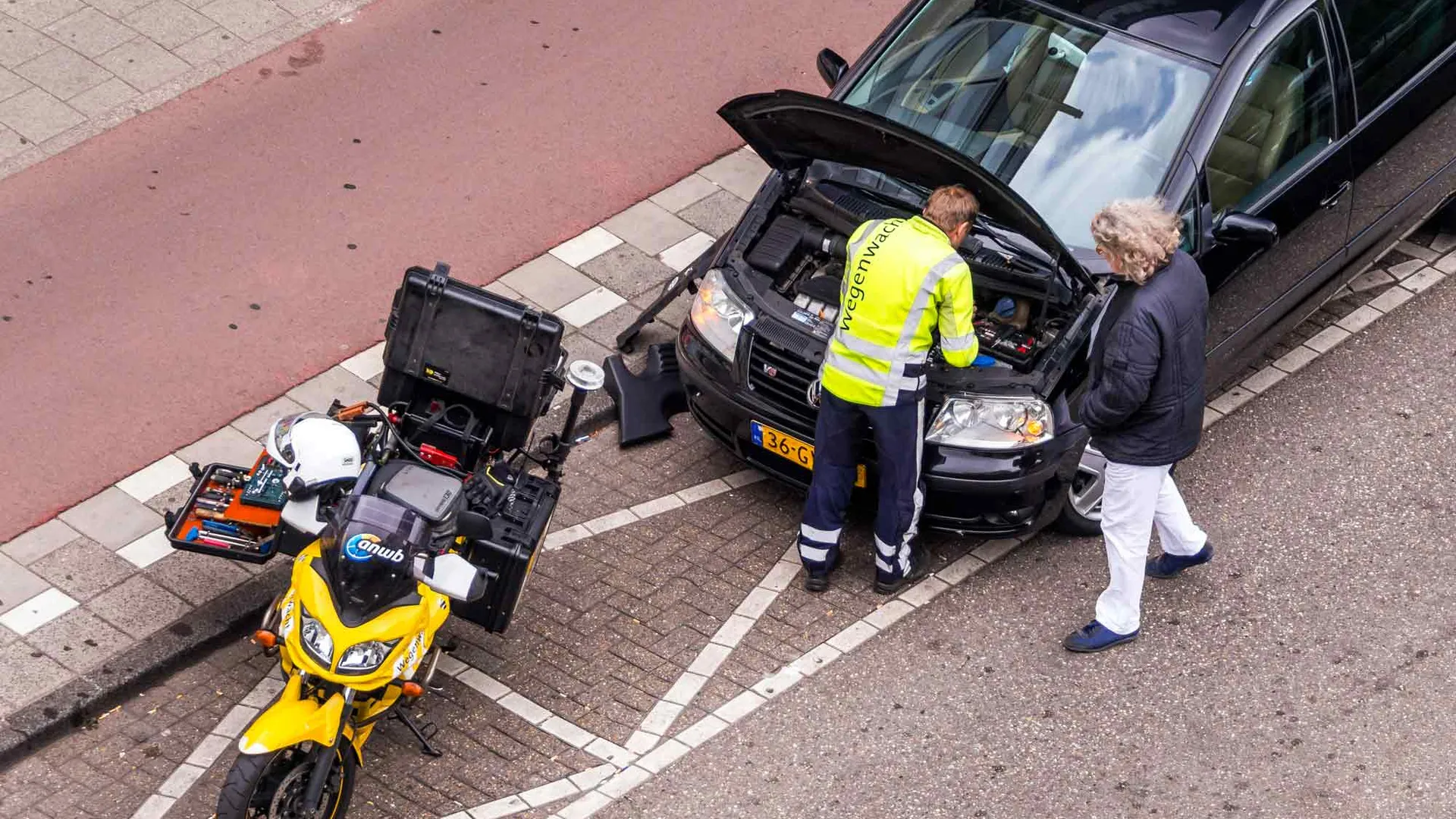 Een anwb wegenwacht monteur repareert een auto van bovenaf gezien